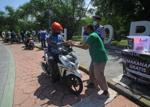 Relawan memberikan bantuan makanan dan minuman gratis kepada pengendara motor yang melintas di Bundaran Institut Teknologi Sepuluh Nopember (ITS), Surabaya, Jawa Timur, Selasa (7/4/2020). Bantuan sebanyak 250-300 bungkus makanan dan minuman gratis yang dibagikan dua hari sekali oleh Yayasan Manarul Ilmi ITS dan Lembaga Manajemen Infaq (LMI) tersebut untuk meringankan beban masyarakat di tengah pandemi COVID-19. NTARA FOTO/Moch Asim/foc.